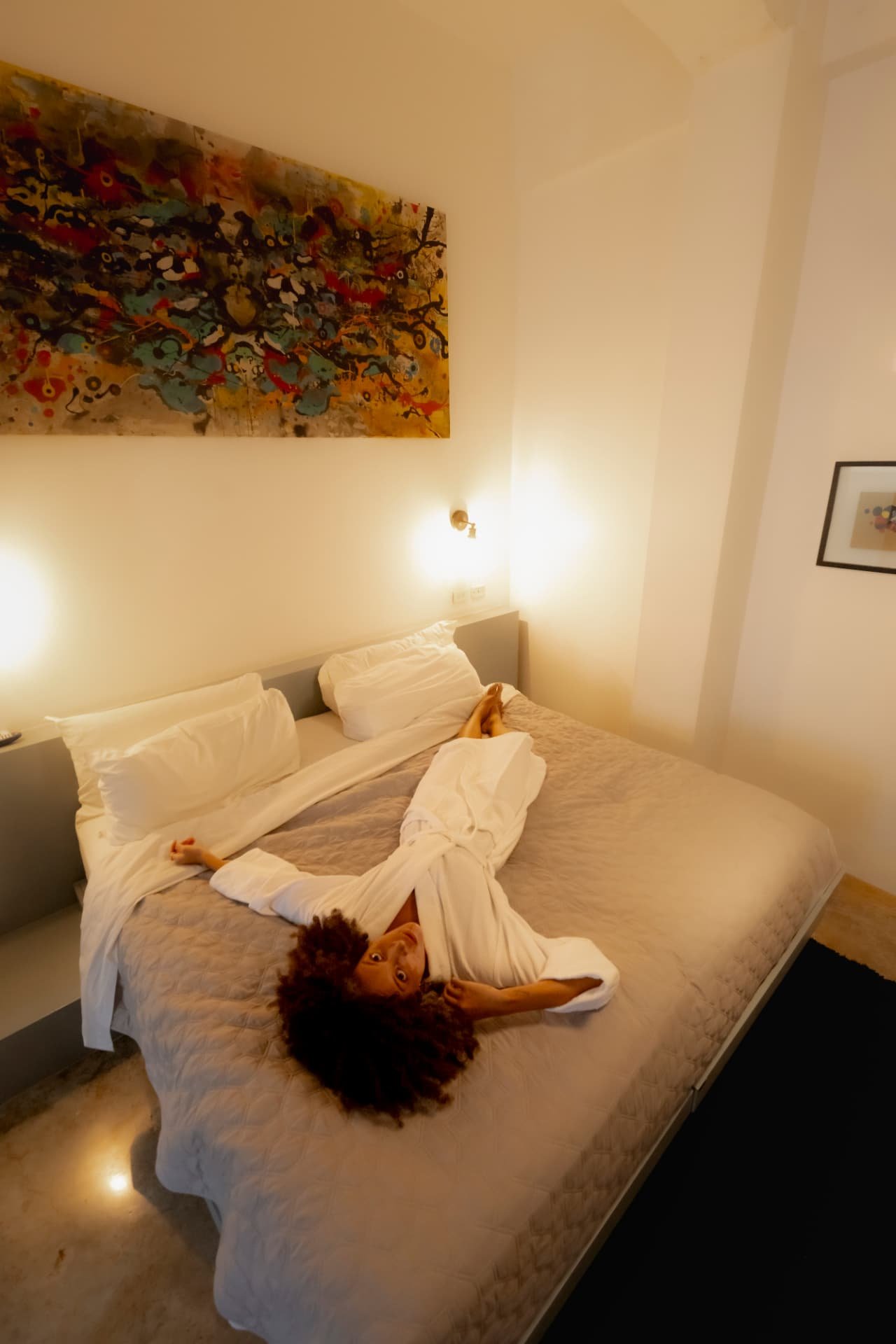Mujer relajada en la cama bajo una obra de arte en una habitación de Tántalo